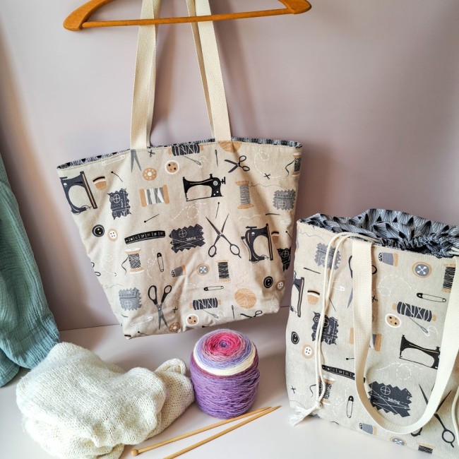 sac-ouvrage-travaux-aiguilles-angelique-la-fee-en-fil 2 sacs à ouvrage Louise sur une table imprimé couture. Devant des aiguilles à tricoter, une pelote de laine et un tricot. Création Angélique La Fée En Fil