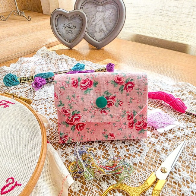 Mini poubelle à fils pliable en tissu rose imprimé de petites roses avec bouton-pression vert, posée sur un napperon en dentelle avec accessoires de broderie, création artisanale Angélique La Fée En Fil.