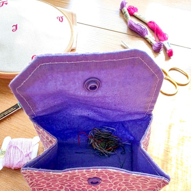 Vue plongée sur l'intérieur ouvert d'une mini poubelle à fils de table dépliante broderie modèle Lavande avec sa doublure violet uni contenant un petit tas de chutes de fils, tissu extérieur coton violet à motifs feuillage, création artisanale Angélique L