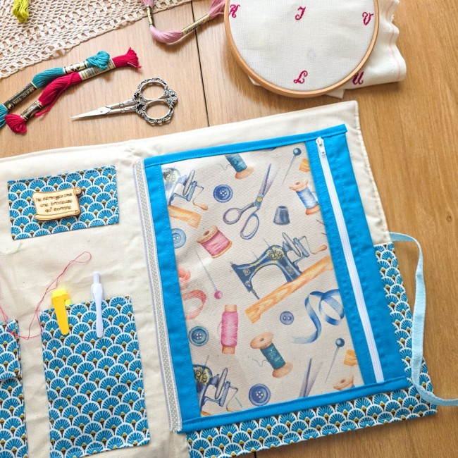 trousse-brodeuse-pochette-zippee-vinyle-mains-et-merveilles-angelique-la-fee-en-fil Vue intérieure de la trousse de brodeuse Mains et Merveilles ouverte avec sa pochette zippée en vinyle transparent bordée de bleu turquoise, révélant le tissu mercerie vintage en fond, création artisanale Angélique La Fée En Fil.