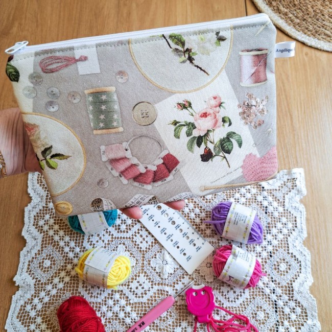 trousse-zippee-motif-couture-broderie-angelique-la-fee-en-fil trousse zippée motif couture dans la main de la créatrice. Sur la table est posé un napperon et des pelotes de laines