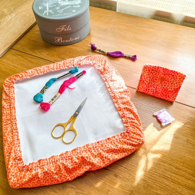 set-ensemble-grime-guard-et-poubelle-a-fils-mandarine-orange-broderie-angelique-la-fee-en-fil Vue d'ensemble d'un set assorti modèle Mandarine comprenant un grime guard housse protège-toile sur cadre et une mini poubelle à fils de table pliante en tissu coton orange à motifs gouttelettes blanches, avec boîte de couture, ciseaux et échevettes, créa