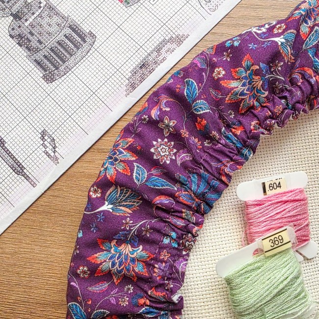 Gros plan sur la fronce et les détails du tissu violet aux motifs floraux et cachemire du grime guard modèle Cachemire, avec cartonnettes de fils et grille de broderie, création artisanale Angélique La Fée En Fil.