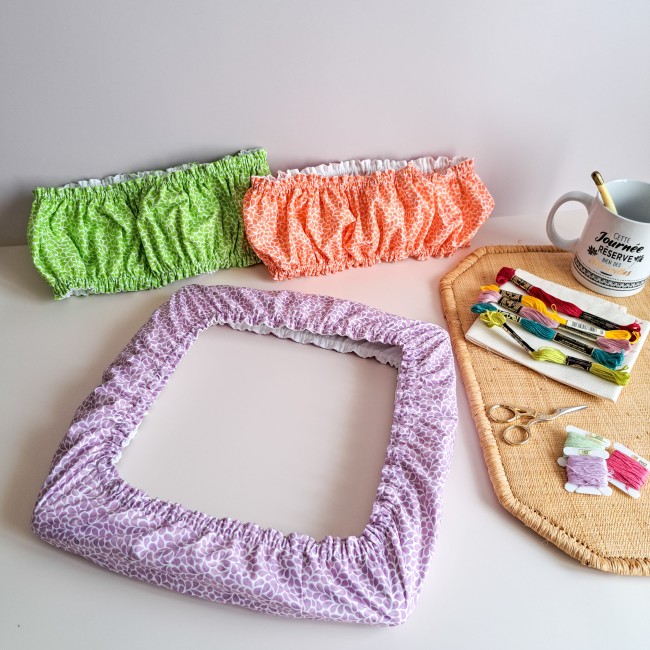 Ensemble de trois Grime Guards de la collection Lumière Végétale par Angélique la Fée En Fil : coloris mauve Lavande sur cadre q-snap, vert Verveine et orange Mandarine présentés avec une tasse et des fils à broder