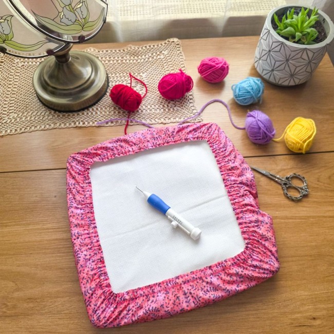 grime-guard-sous-bois-rose-punch-needle-cadre-qsnap-angelique-la-fee-en-fil.jpg Un couvre-cadre (grime guard) rectangulaire modèle Sous-bois Rosé en coton vieux rose à motifs de branches violettes, protégeant une toile Aïda blanche. Une aiguille magique à punch needle bleue et blanche est posée au centre. Décoration créative sur tabl
