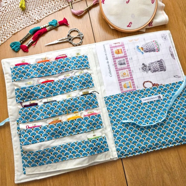 trousse-brodeuse-ouverte-cartonnettes-fils-a-broder-grille-mains-et-merveilles-angelique-la-fee-en-fil Vue d'ensemble de la trousse de brodeuse Mains et Merveilles ouverte à plat, avec rangements pour cartonnettes à motif éventails bleus et grille de broderie insérée, création artisanale Angélique La Fée En Fil