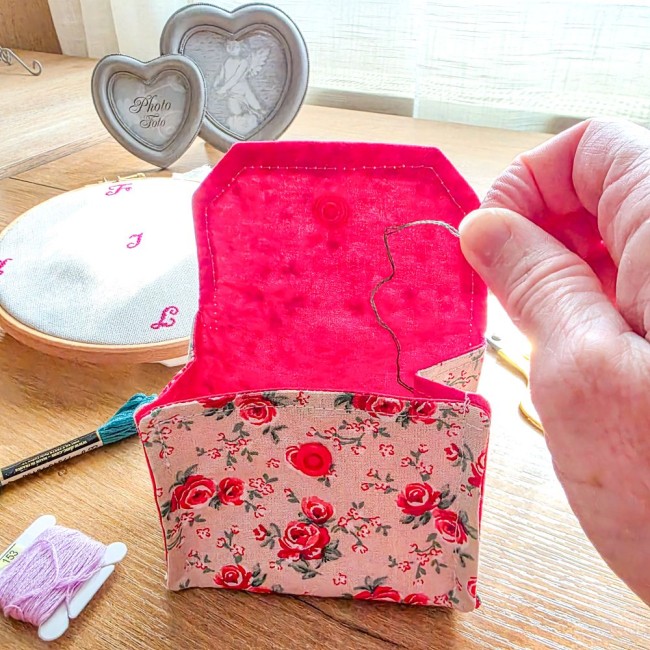 Gros plan d'une mini poubelle à fils ouverte en utilisation modèle Vanille, montrant l'intérieur en tissu rouge fuchsia uni avec dépôt d'un brin de fil de broderie, extérieure en tissu écru effet lin aux motifs bucoliques de roses rouges, création artisan