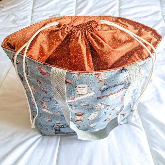sac cabas posé sur un lit. fermé par un lien coulissant. motif du sac accessoire de couture . Création Angélique La Fée En Fil