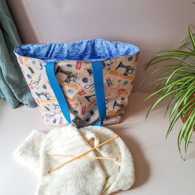posé sur une table, un sac cabas ouvert devant un tricot avec des aiguilles à tricoter. Création Angélique La Fée En Fil