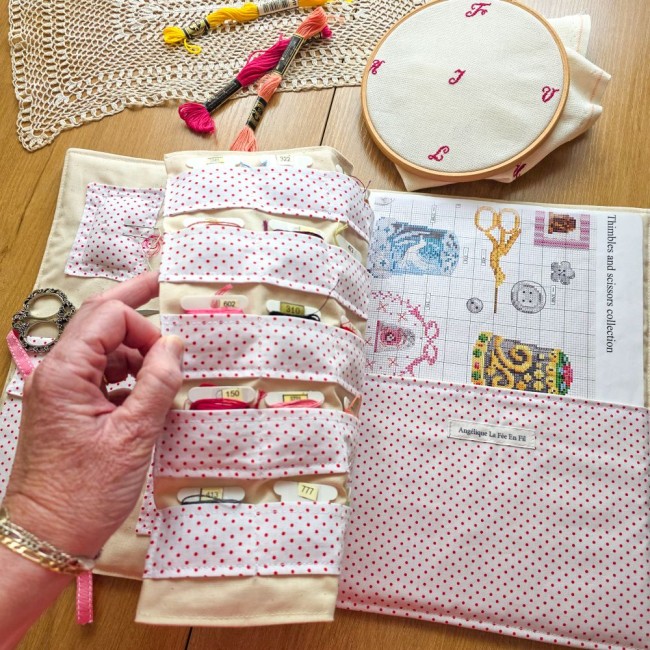 Main tournant le volet intérieur de la trousse de brodeuse Nina à pois roses, dévoilant les multiples rangements pour cartonnettes à fils et la pochette pour diagramme, création artisanale Angélique La Fée En Fil.