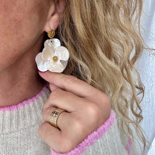 Boucles d’oreilles Iris fleur ivoire et cœur doré portées avec un pull rose et écru