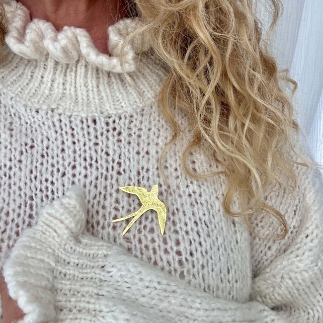 Broche hirondelle dorée portée sur un pull en maille écrue – DEBA CREATION