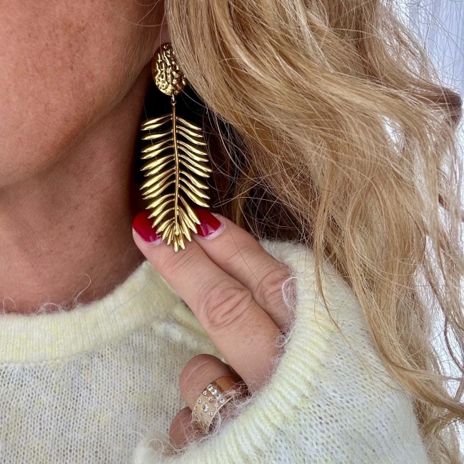 Détail boucle d’oreille dorée Fauve Détail d’une boucle d’oreille dorée feuillage Fauve portée à l’oreille – DEBA CREATION