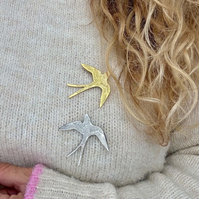 Broches hirondelles dorée et argentée portées sur un pull écru – DEBA CREATION