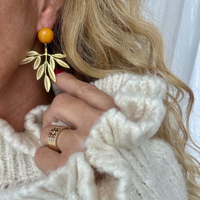 Boucles d’oreilles dorées feuille Florine avec clou rond moutarde, portées à l’oreille – DEBA CREATION