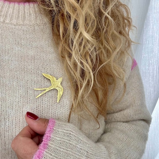 Détail de la broche hirondelle dorée portée sur un pull écru – DEBA CREATION