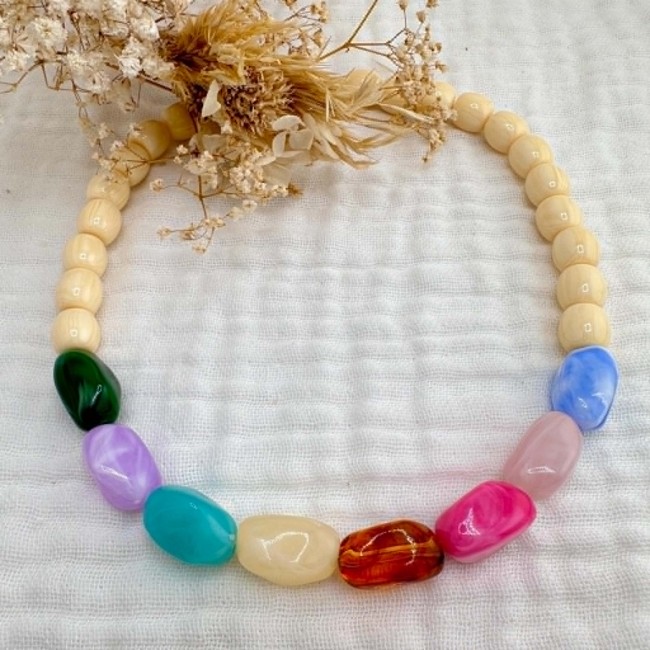 Collier Happy en perles multicolores présenté à plat avec fleurs séchées