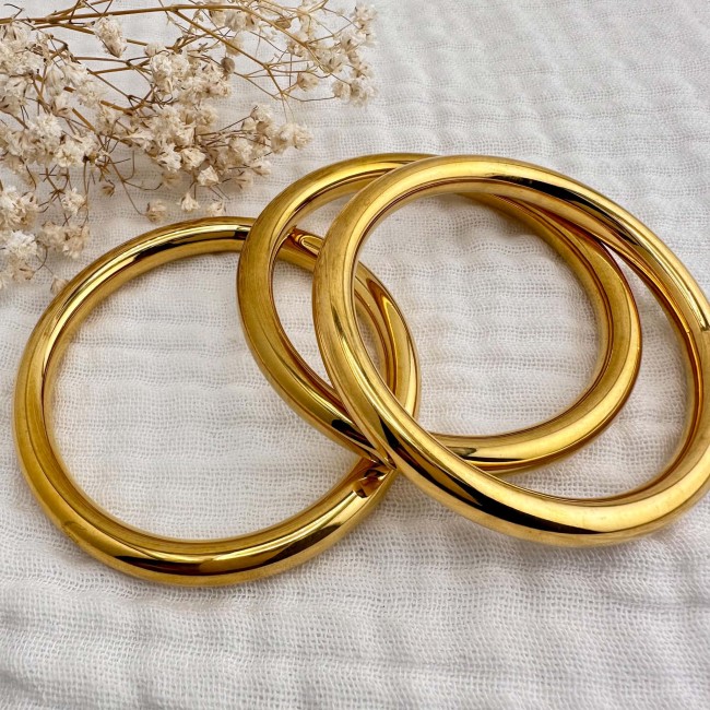 Plusieurs bracelets joncs dorés présentés sur un fond écru