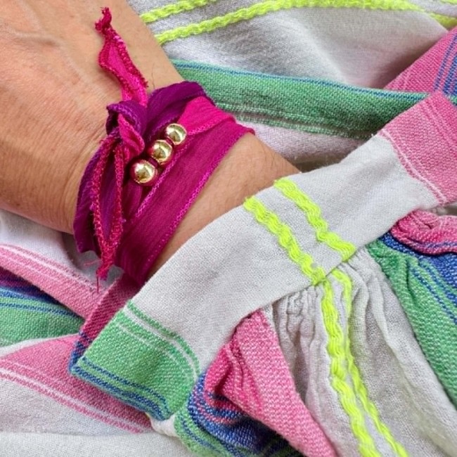 Bracelet bohème Annick en soie rose fuchsia avec trois perles dorées porté au poignet
