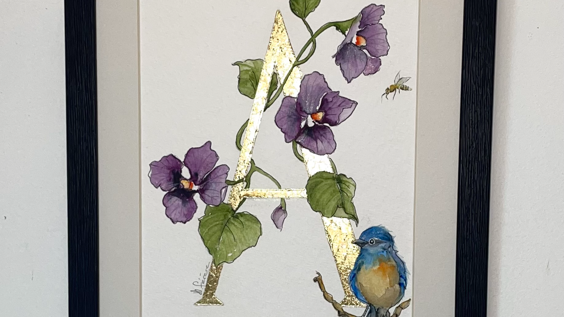 Initiale peinte à la main d'une feuille d'or entourée d'un décor de violettes et d'un oiseau à l'aquarelle