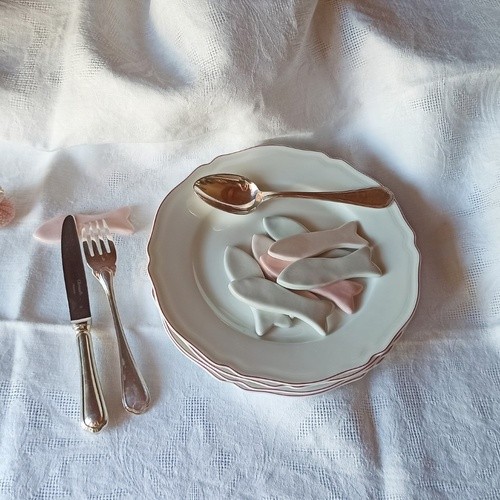 Porte-couteaux en porcelaine en forme de poissons, faits main, présentés sur une table aux inspirations marines avec assiettes anciennes et couverts en argent.
