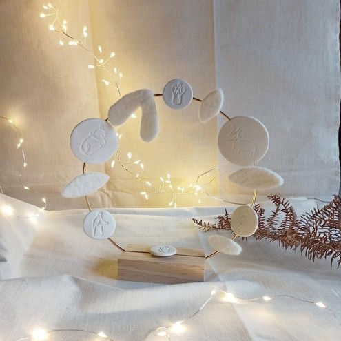 Couronne de Noël en porcelaine faite main, décorée de médaillons blancs en céramique représentant la crèche, présentée sur un support cercle doré.