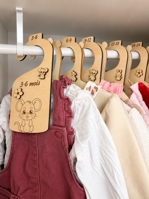 Séparateurs penderie bébé en situation Séparateurs de tailles bébé en bois installés dans une penderie avec vêtements suspendus