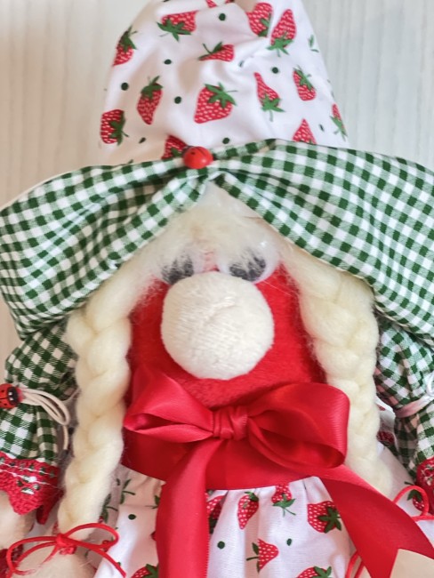 detail-visage-poupee-fraise-fait-main Gros plan sur le visage, les nattes blondes et le grand nœud rouge satiné de la poupée fraise artisanale.
