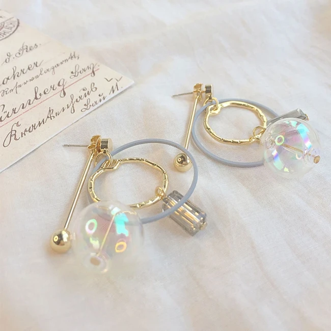 Boucles d'oreilles anneau doré et perle irisée posées sur tissu