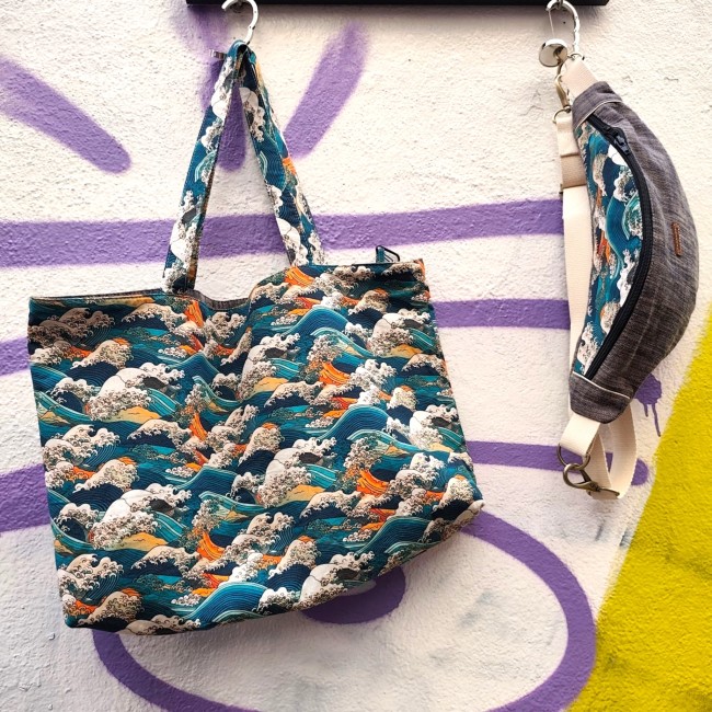 sac cabas et sac banane suspendus à des crochets dans la rue devant un mur jaune et blanc tagué en violet