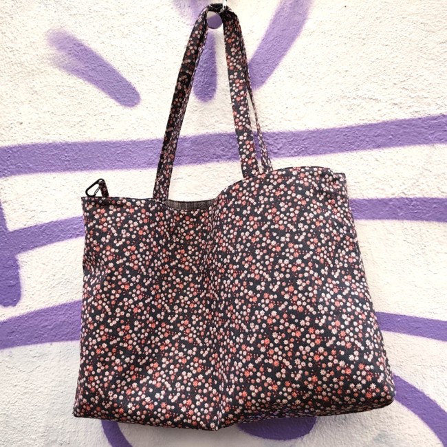 Accessoires textiles de qualité fabriqués à Marseille - Artisanat local - Jéjé & Lulu un sac cabas plein de petites fleurs roses suspendu devant un mur blanc avec des graffitis violet dans une rue de marseille