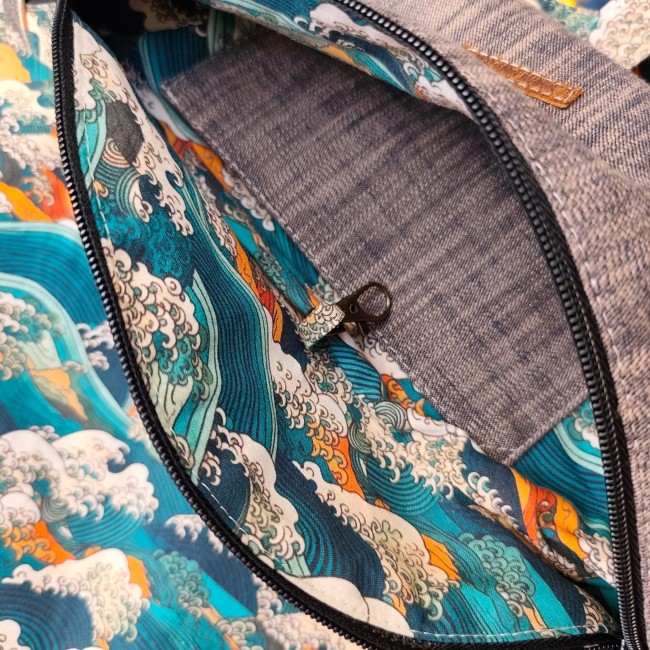 focus sur les détails d'un sac banane. Poche intétieure en chambray et doublure en tissu motif vague kanagawa bleu sarcelle, écru et nuances orange. On peut voir un petit mousqueton. La fermeture éclair noire est ouverte.