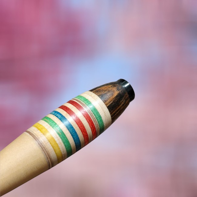 zoom sur le haut d' un stylo en bois où on peut voir des rayures en bois bleues vertes jaunes marron rouge et sur la partie haute du bois marron foncé avec un veinage très prononcé