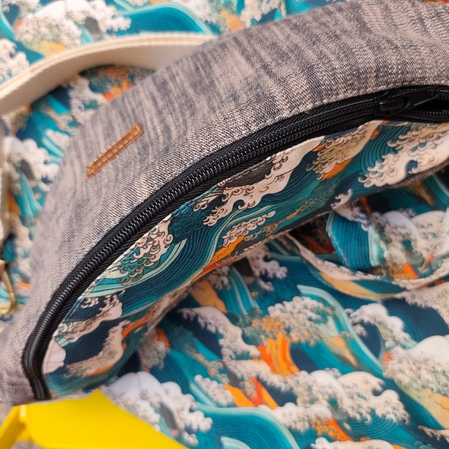 zoom sur un sac banane fermé posé sur un beau tissu avec les motifs de la vague d' Hokusaï. On aperçoit un bout de sangle écru et une petit étiquette rectangulaire en simili cuir gravé Jéjé & Lulu