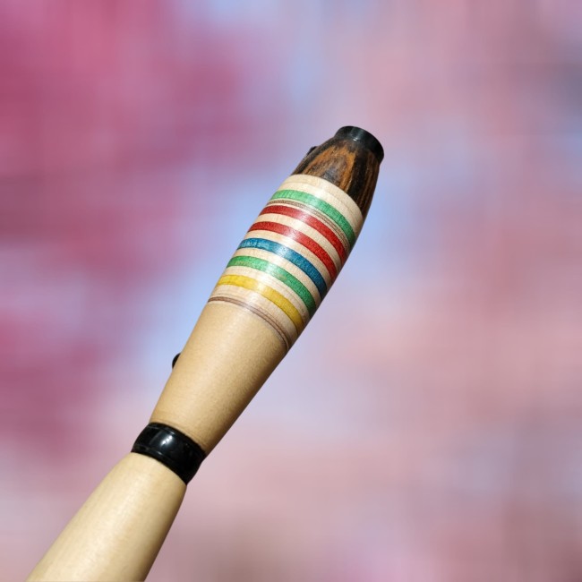 zoom sur le haut d' un stylo en bois où on peut voir des rayures en bois bleues vertes jaunes marron rouge et sur la partie haute du bois marron foncé avec un veinage très prononcé