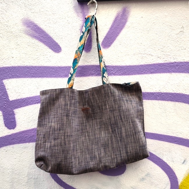 sac cabas réversible Kanagawa fabriqué à Marseille - Artisanat local Jéjé & Lulu Sac rectangulaire en chambray avec des anses colorées accroché à une pancarte sur un mur blanc tagué