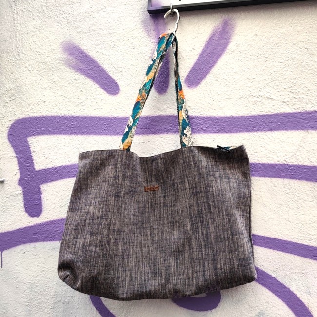 sac cabas réversible Kanagawa fabriqué à Marseille - Artisanat local Jéjé & Lulu Sac rectangulaire en chambray avec des anses colorées accroché à une pancarte sur un mur blanc tagué
