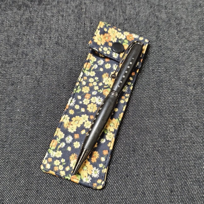 accessoires de papeterie fait mainen tissu - made in france - jéjé lulu trousse pour deux stylos fleuries - petites fleurs jaunes orange sur fond noir - aux couleurs de l'automne avec dessus un stylo en bois noir ébène avec des incrsutations d'étain