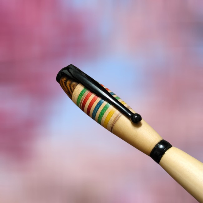 zoom sur le haut d' un stylo en bois où on peut voir des rayures en bois bleues vertes jaunes marron rouge et sur la partie haute du bois marron foncé avec un veinage très prononcé