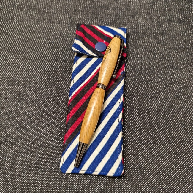 stylo en bois gravé posé sur une mini trousse en tissu wax à rayures bleu marine  bordeaux et blanches