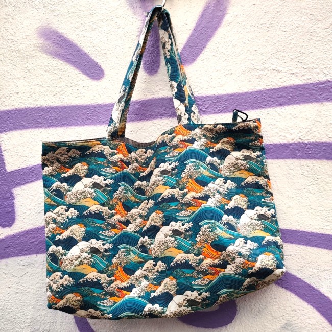 sac cabas réversible Kanagawa fabriqué à Marseille - Artisanat local Jéjé & Lulu Sac cabas en tissu motifs japonais vague de Kanagawa d'hokusaï de couleurs bleu sarcelle, écru, rouge orange suspendu avec un crochet à un mur blanc avec des tags violet