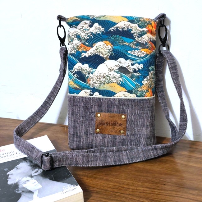 une belle pochette livre en tissu  qui se transforme en sac. Elle a une poche avant décorée avec du passepoil lurex doré. Sur cette poche, une étquette gravée Jéjé & Lulu. A gauche un livre d' Oscar wilde le portrait de Dorian Gray chez Folio