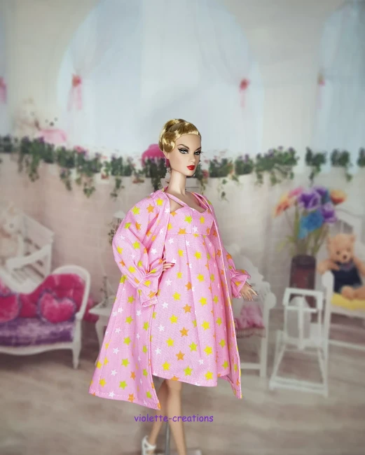 Poupée Barbie portant un ensemble de nuit rose avec motif étoiles jaunes et blanches, incluant une robe de chambre à volants.