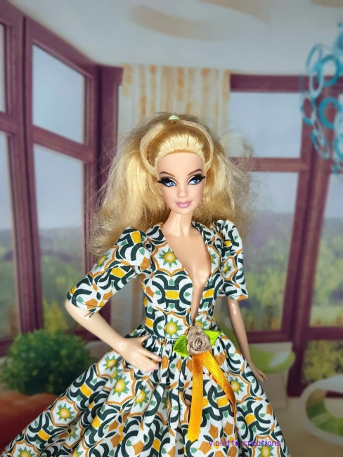 Robe de galla longue pour poupée type Barbie en coton, motif mosaïque géométrique vert émeraude et ocre sur fond écru, décolleté V, manches bouffantes, blason doré et ruban de velours ocre à la taille, création artisanale par Violette-Creations.