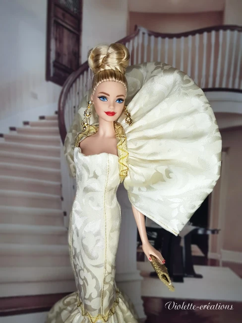 Poupée Barbie de collection en robe de soirée sirène dorée et argentée, posant dans un salon de luxe feutré avec chandeliers.