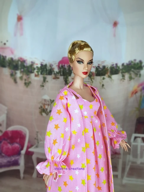 Poupée Barbie portant un ensemble de nuit rose avec motif étoiles jaunes et blanches, incluant une robe de chambre à volants.