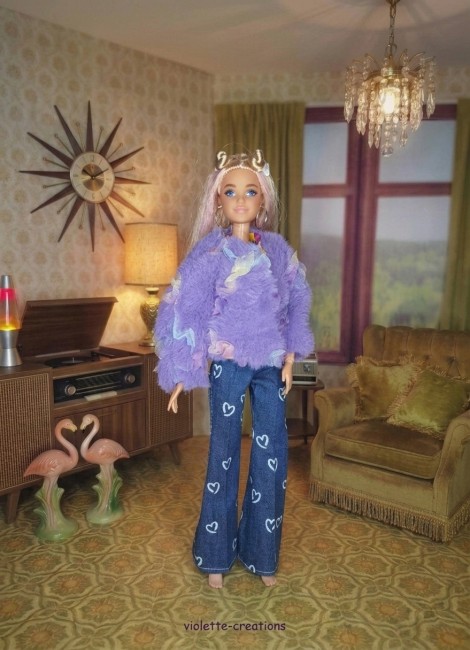 Poupée Barbie portant un jean bleu à cœurs, un maillot rose fushia, un blouson violet décoré de papillons et un t-shirt à motif sous le blouson.