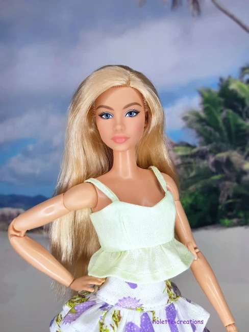 Tenue artisanale pour poupée Barbie avec crop top vert pastel et mini-jupe à volants motif fleurs violettes, style estival.