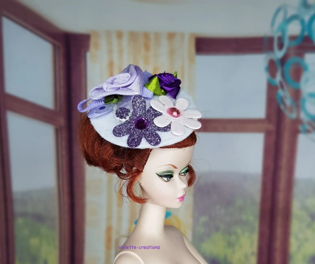 Chapeau bibi lilas pour poupée type barbie avec roses en ruban, fleurs pailletées et perles blanches.