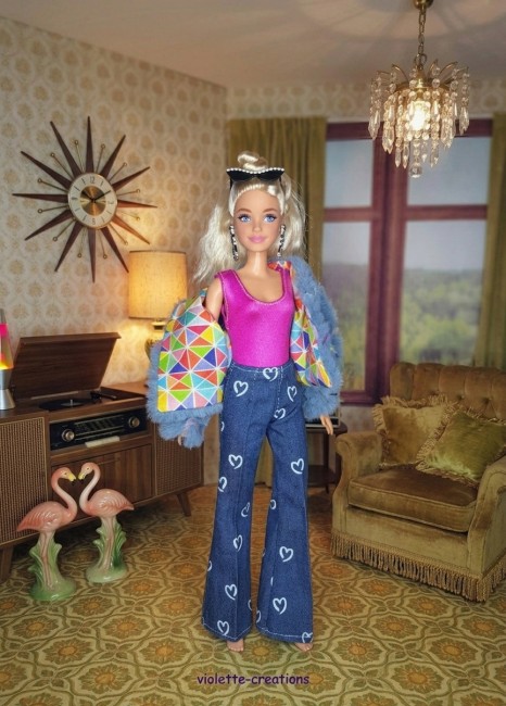 Poupée Barbie portant un jean bleu à cœurs, un maillot rose fushia, un blouson violet décoré de papillons et un t-shirt à motif sous le blouson.